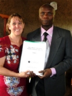 Pastor Laura presenting Pastor Tom the Bundibugyo KIMI coordinator with his KIMI curriculum