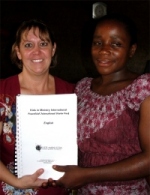 Pastor Laura presenting Pastor Tom's wife the Bundibugyo school teacher with her KIMI curriculum